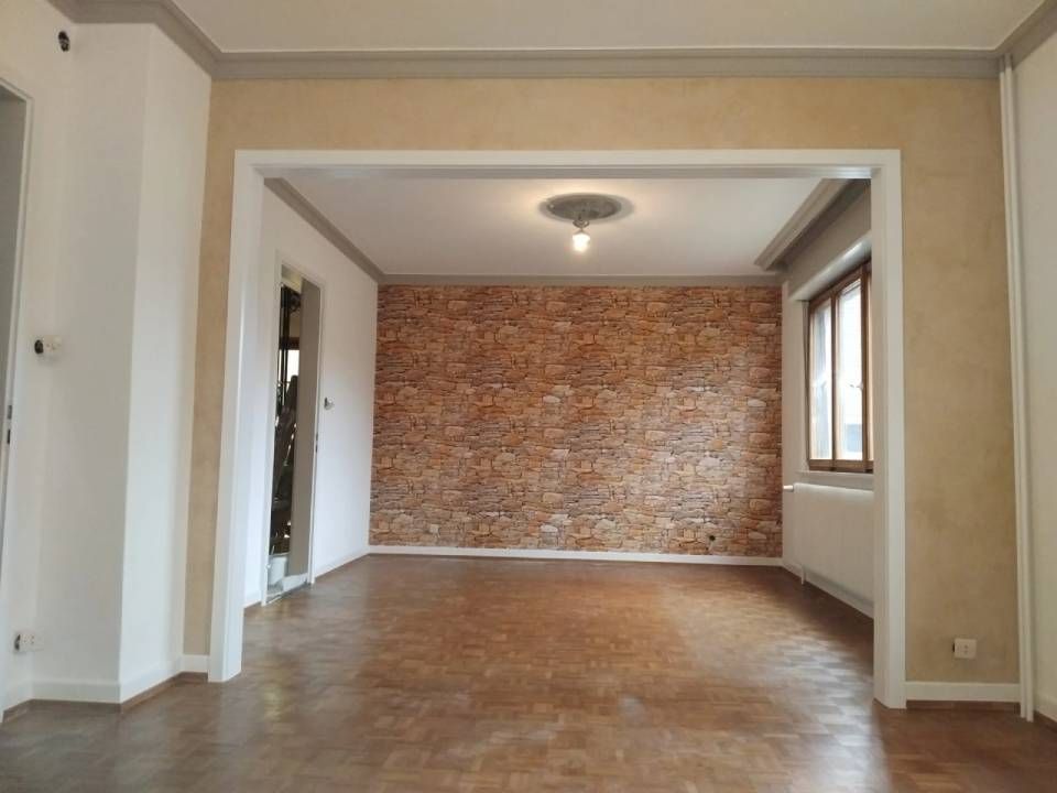 Pièce vide avec mur en pierre, luminaire, porte et parquet.