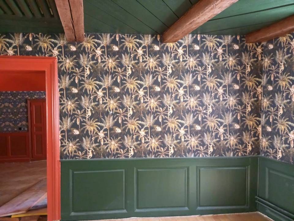 Pièce avec lambris et plafond vert foncé, papier peint à motifs floraux et encadrement de porte rouge.
