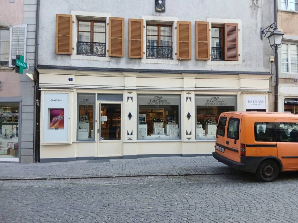 Extérieur d'une bijouterie avec une camionnette orange garée dans une rue pavée.