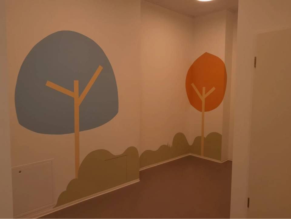 Pièce intérieure décorée d'arbres de style dessin animé peints : bleu et orange sur murs blancs, sol marron.