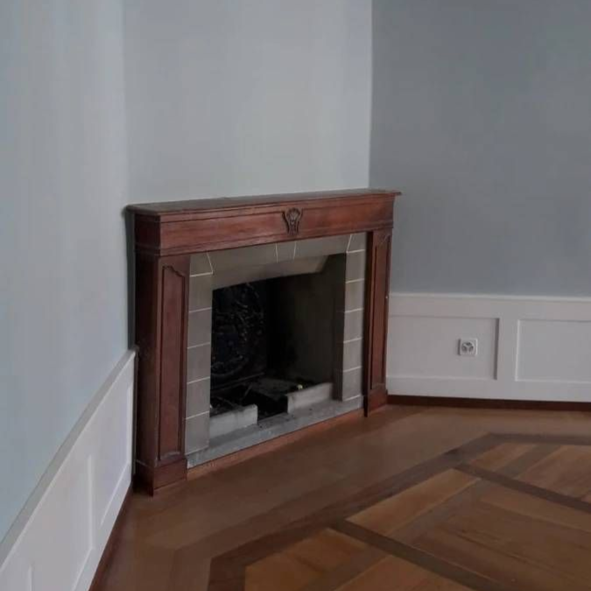 Coin d'une pièce avec une cheminée en bois, des murs bleu clair et un parquet à motifs.