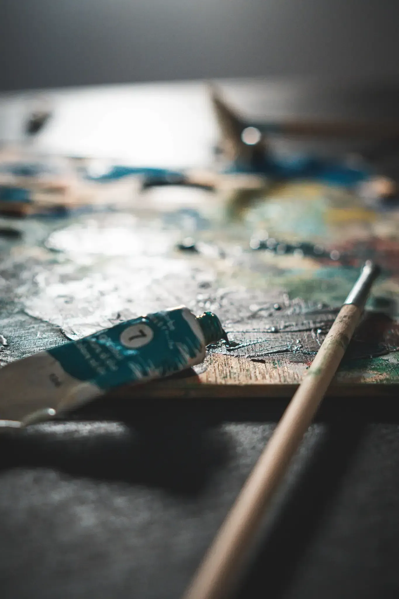 Tubo de pintura, pincel y salpicaduras de pintura de colores en una paleta.