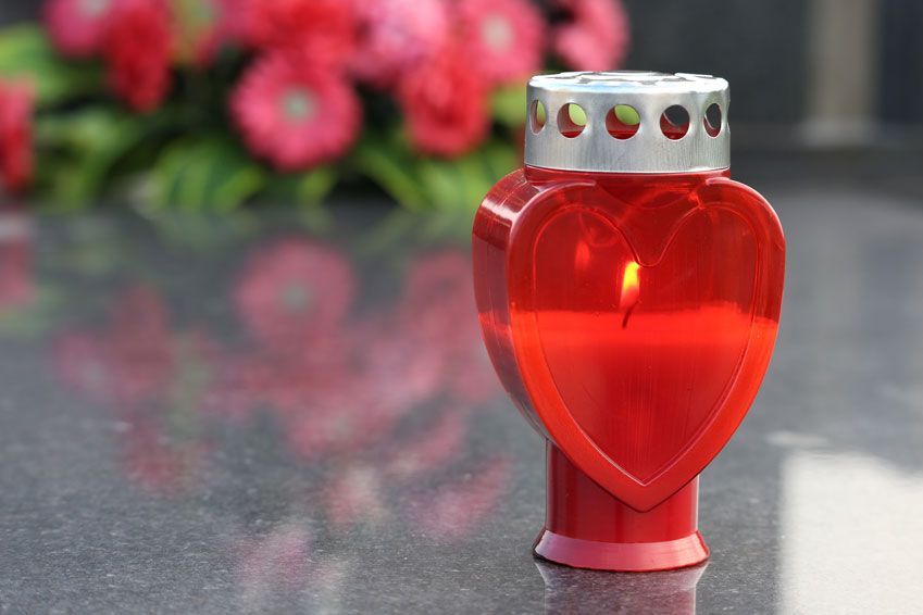 Eine rote herzförmige Kerze wird vor Blumen angezündet