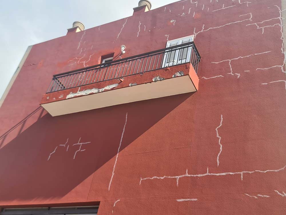 Exterior de edificio rojo con muchas grietas blancas, un pequeño balcón y sol visible.