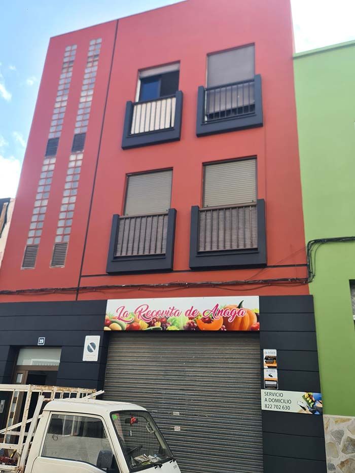 Edificio rojo y negro con una frutería en la planta baja. Balcones y ventanales adornan los pisos superiores.