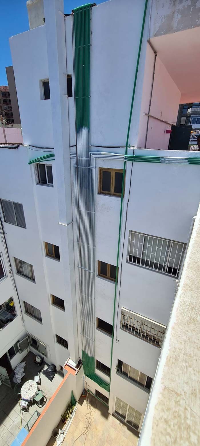 Exterior del edificio blanco con detalles verdes, visto desde arriba. Se aprecian ventanas y balcones en la fachada.