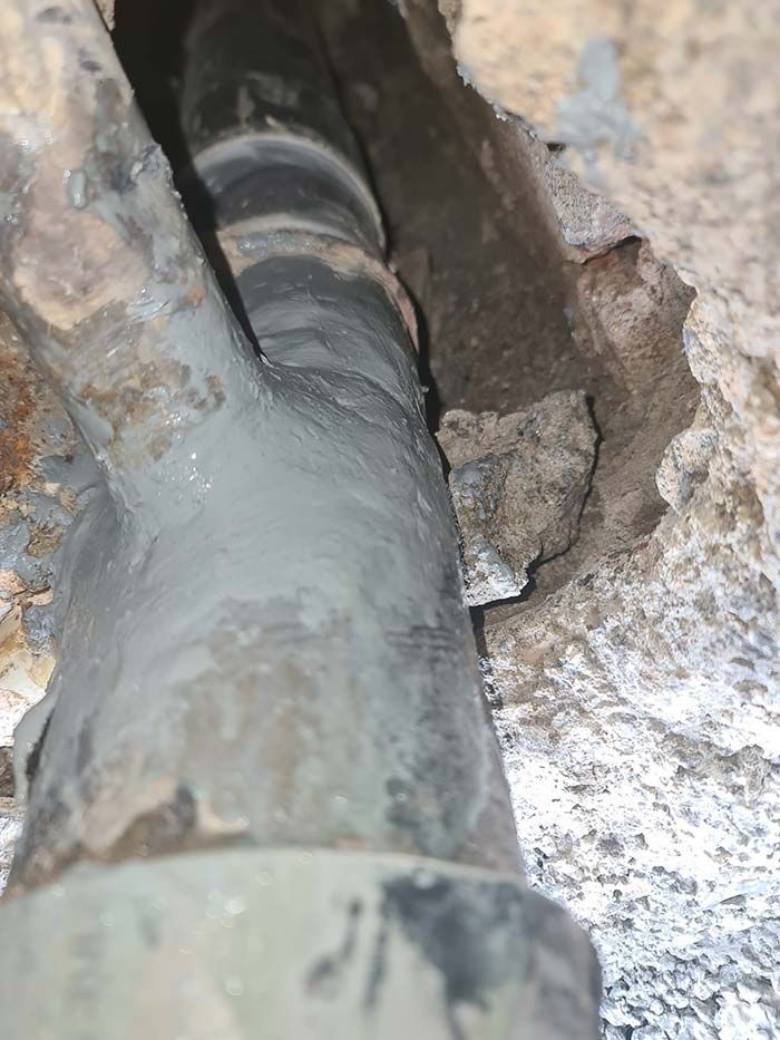 Primer plano de tuberías antiguas selladas con cemento gris dentro de un muro de piedra. Una tubería más pequeña se ramifica.