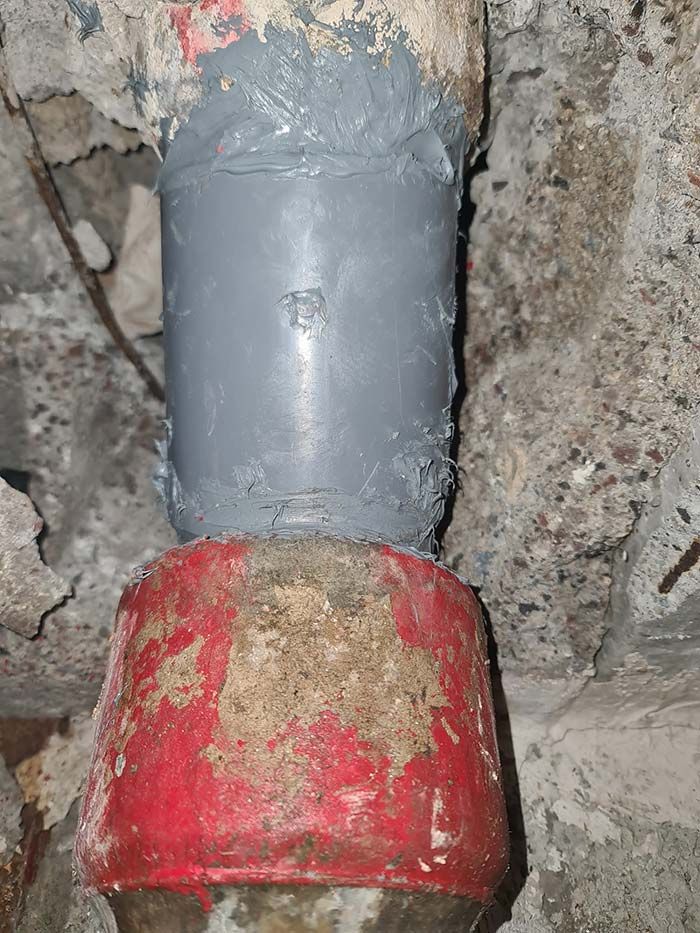 Una unión de tubería revestida con sellador gris, que se conecta a una sección de tubería con tapa roja, sobre un fondo de hormigón.