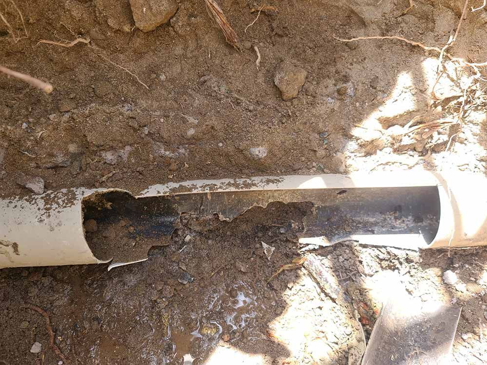 Tubería de plástico dañada expuesta en una zanja de tierra, con trozos de tubería faltantes.