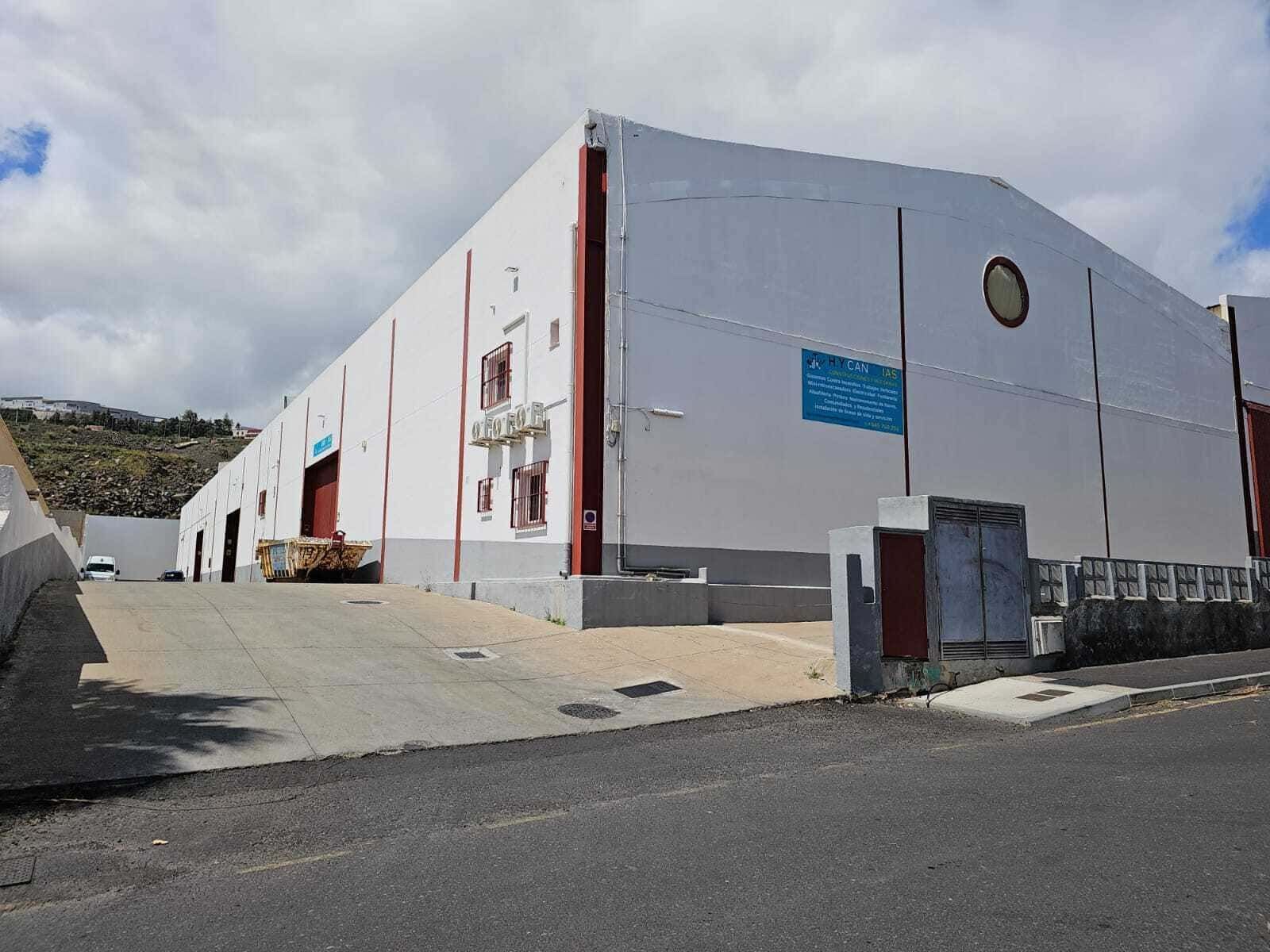 Un almacén industrial blanco con una rampa de carga bajo un cielo nublado.