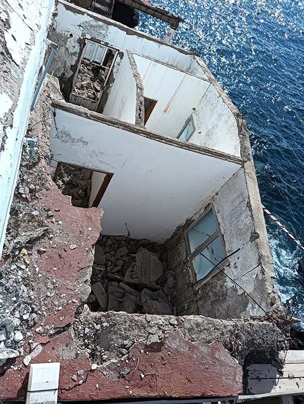 Edificio demolido con habitaciones visibles y paredes abiertas, cerca de un cuerpo de agua. La estructura presenta daños.