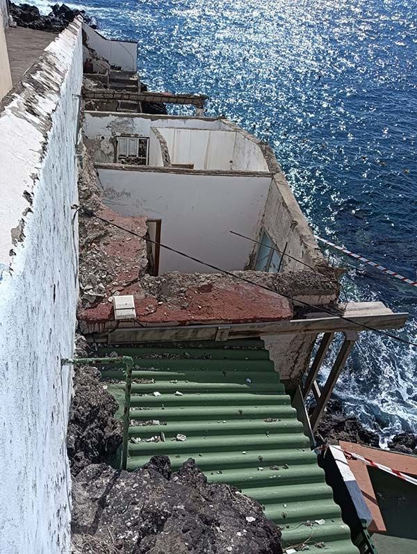 Edificio en ruinas sobre un acantilado rocoso con vistas al océano. Unas escaleras verdes descienden del edificio.