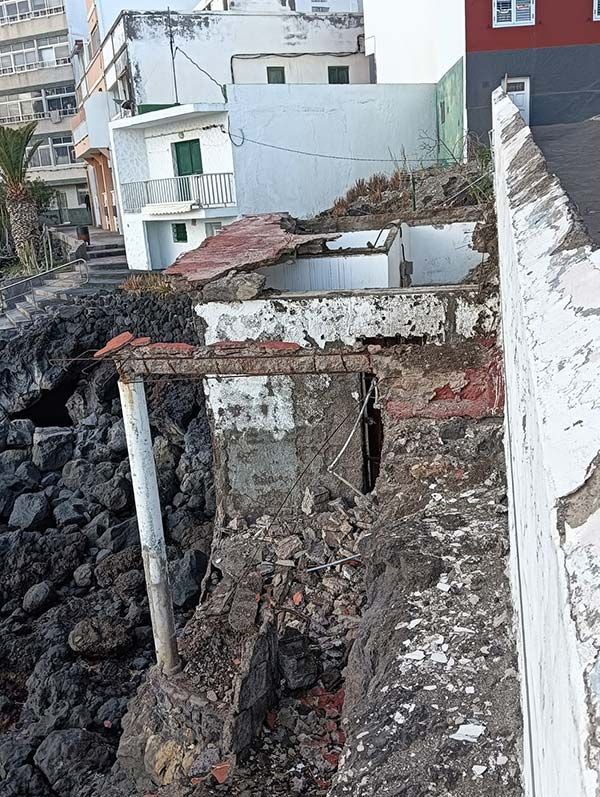 Daños en edificios al borde de un acantilado rocoso. Edificios blancos y grises con ladrillos a la vista, algunos derrumbándose.