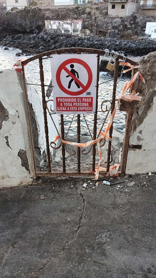 Puerta metálica que bloquea el acceso a una costa rocosa, con una señal de