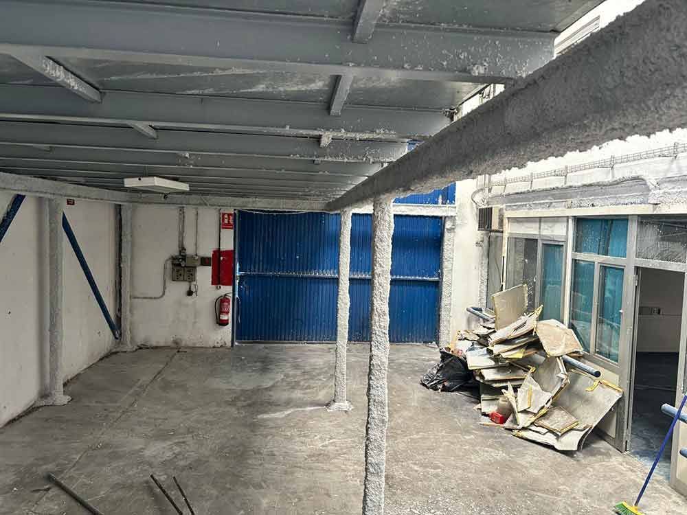 Interior de un local comercial con vigas metálicas expuestas, paredes grises, una puerta azul y un montón de escombros.