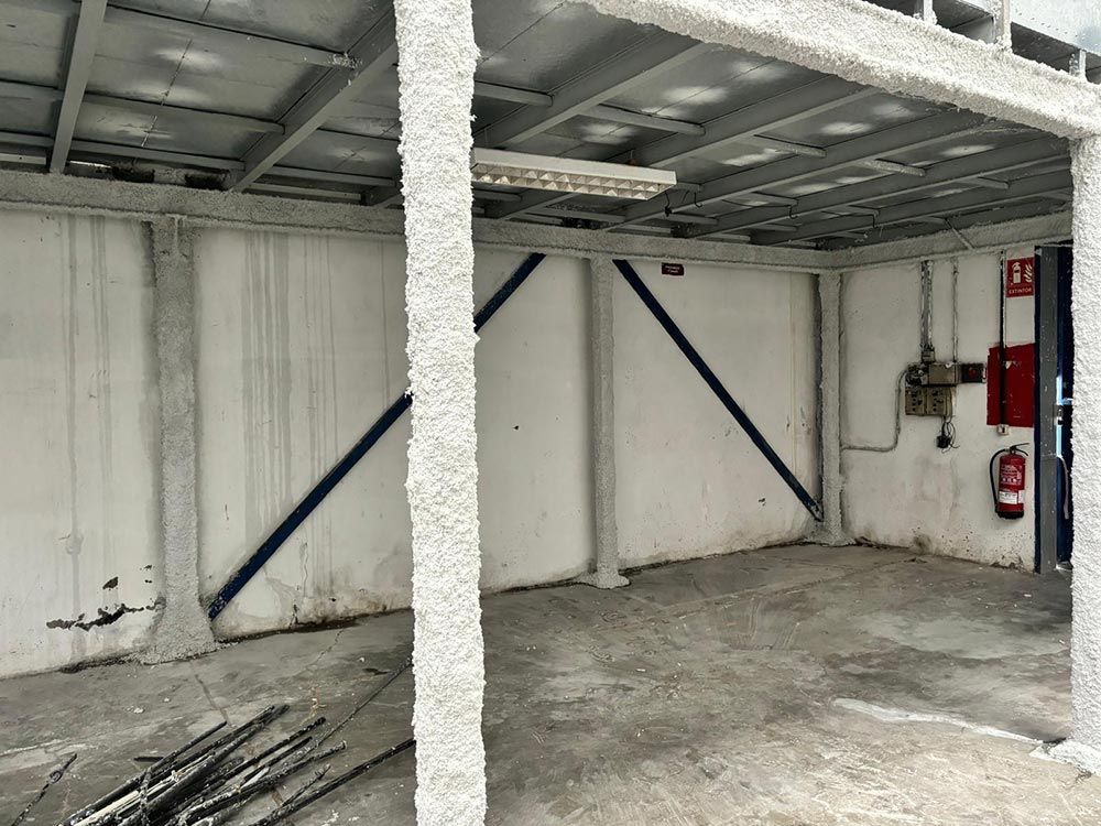 Interior de una habitación de hormigón con techo de metal, tirantes diagonales azules y un extintor de incendios rojo.