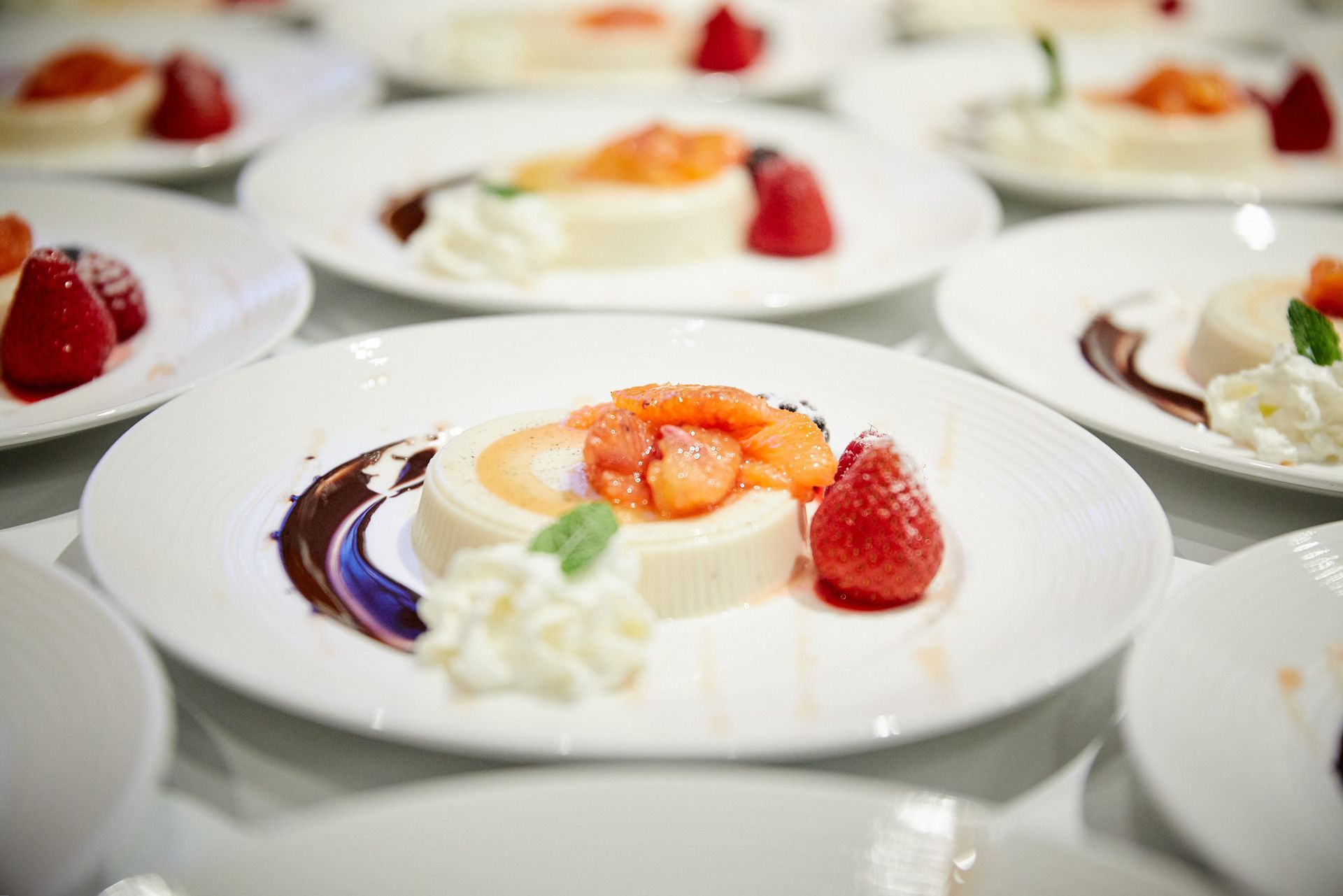 Tellerdessert: Weiße Panna Cotta mit Orangenscheiben, Erdbeere, Schokoladensauce und Schlagsahne.