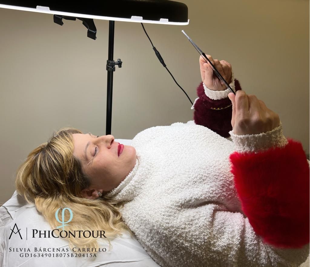 Mujer recibiendo un procedimiento cosmético, acostada en una mesa bajo una luz brillante, sosteniendo un instrumento.