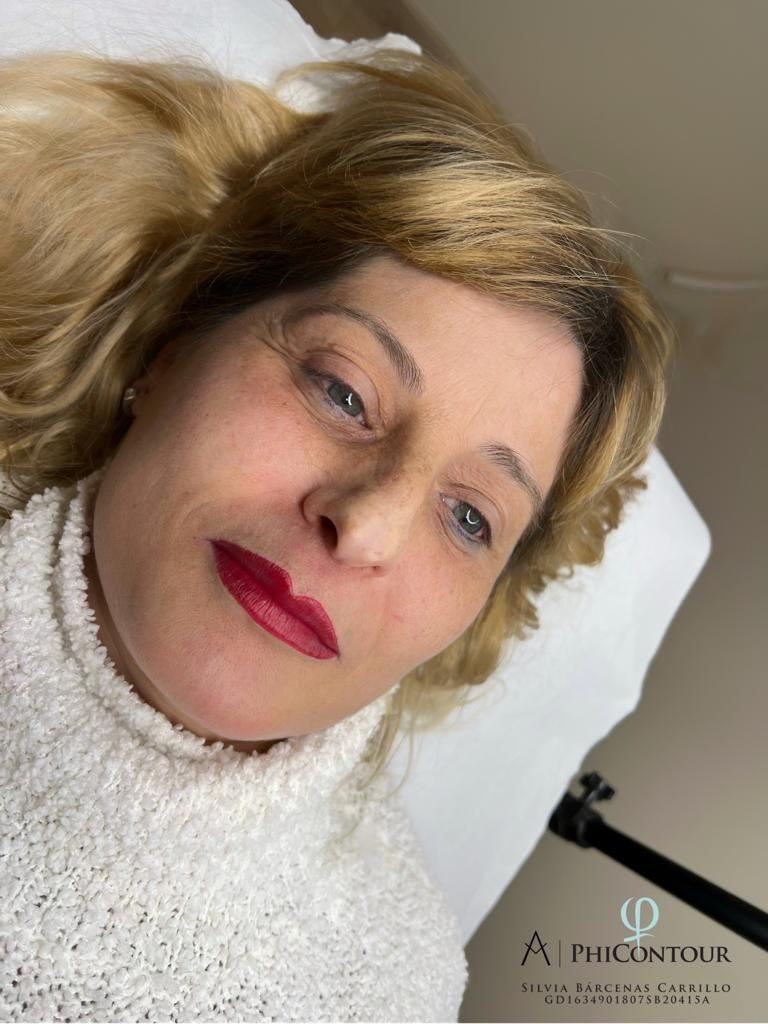Mujer con maquillaje de labios rojo, acostada sobre una superficie blanca, vistiendo un suéter blanco con textura.