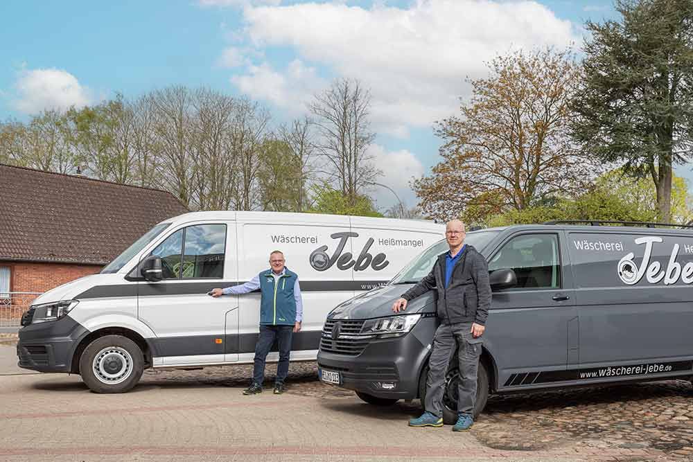 Zwei Männer stehen neben zwei Lieferwagen auf einem Parkplatz.