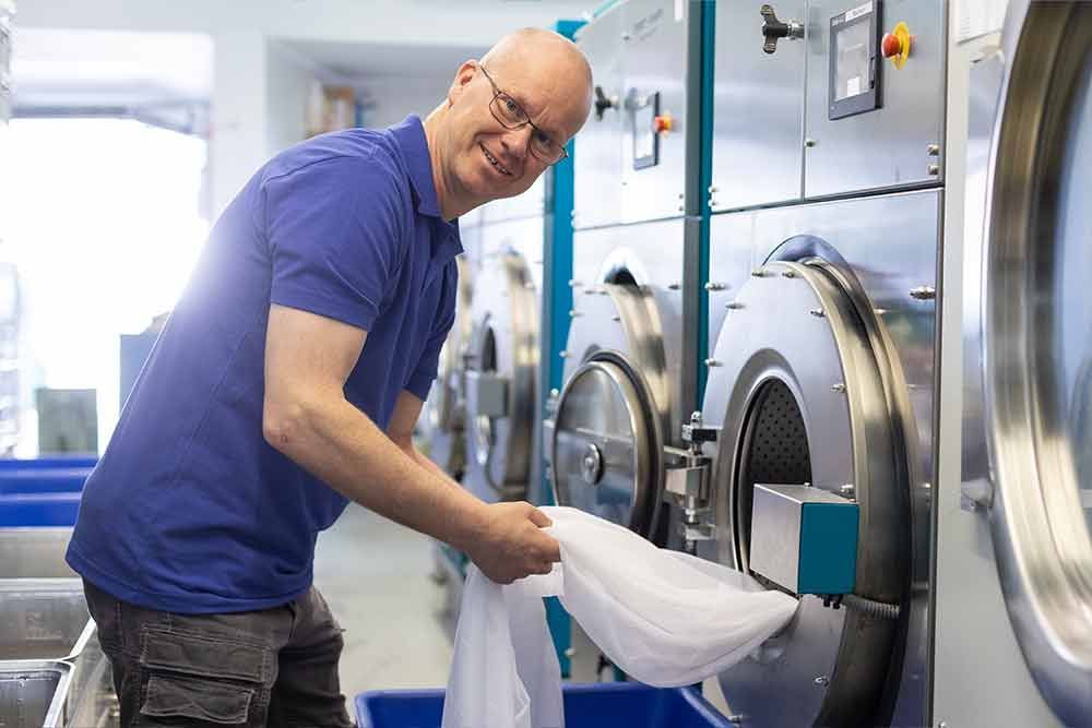Ein Mann steckt in einem Waschsalon Wäsche in eine Waschmaschine.