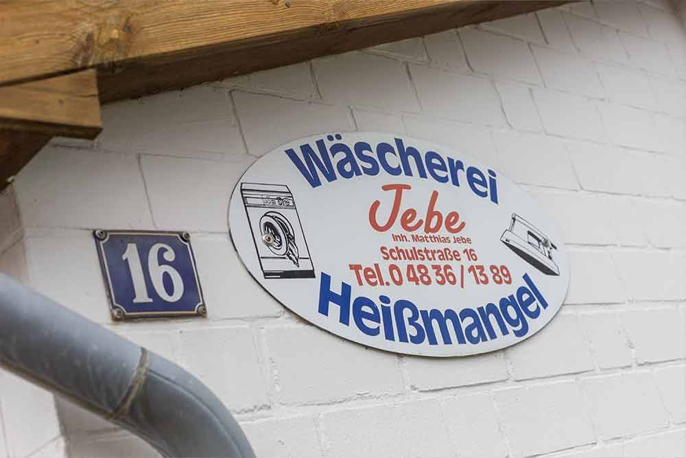 Ein Schild an der Seite eines Gebäudes mit der Aufschrift „Wascherei Jebe“