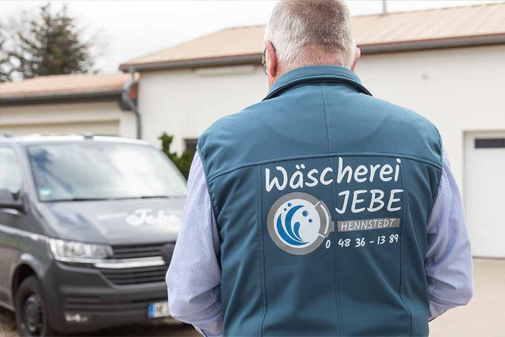 Ein Mann in einer blauen Weste steht vor einem Lieferwagen.