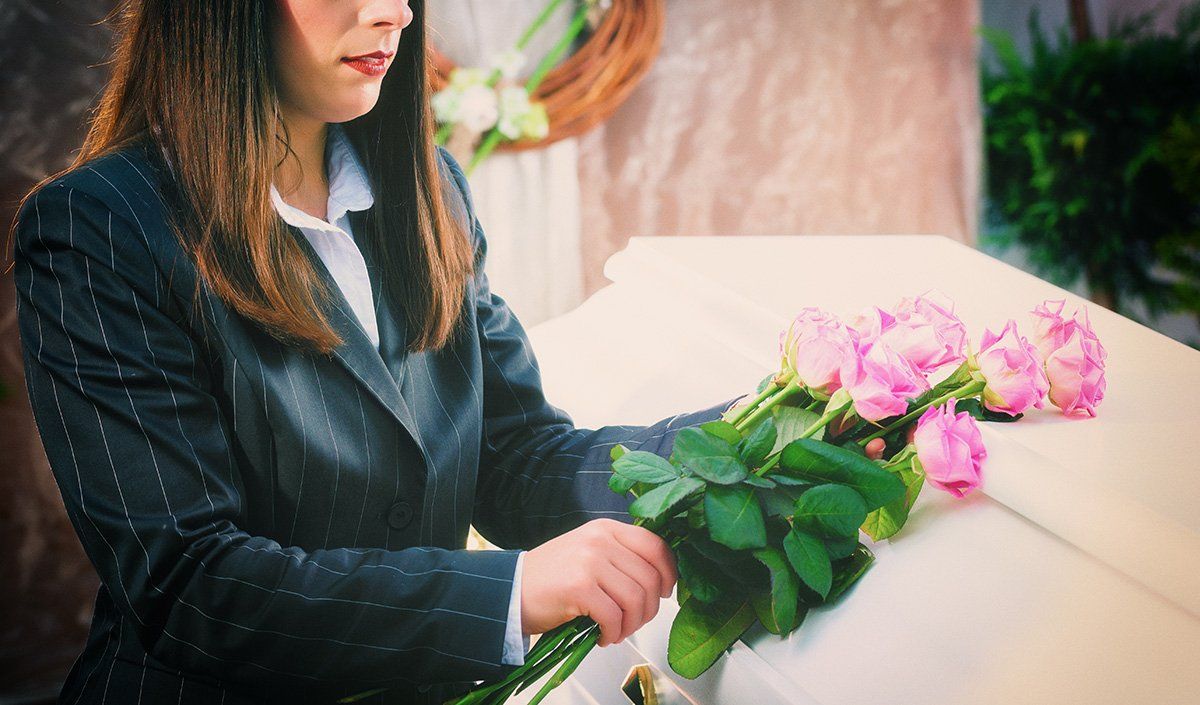 Femme vêtue de noir se tenant devant un cercueil avec des roses roses dans les mains