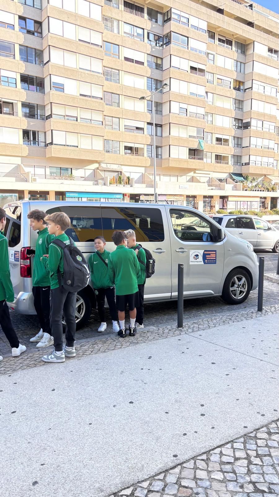 Grupo de pessoas vestindo camisas verdes perto de uma van prateada, em frente a um prédio.