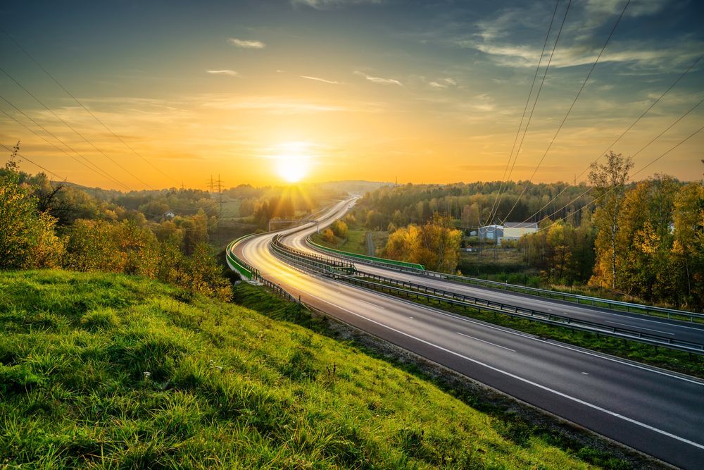 Carretera serpenteando a través de verdes colinas al atardecer, con el sol brillando intensamente.