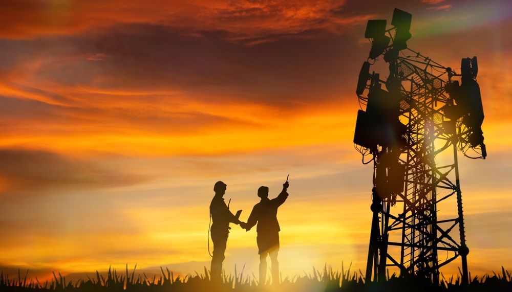 Siluetas junto a una torre de comunicaciones al atardecer. Dos personas señalando, cielo dorado.