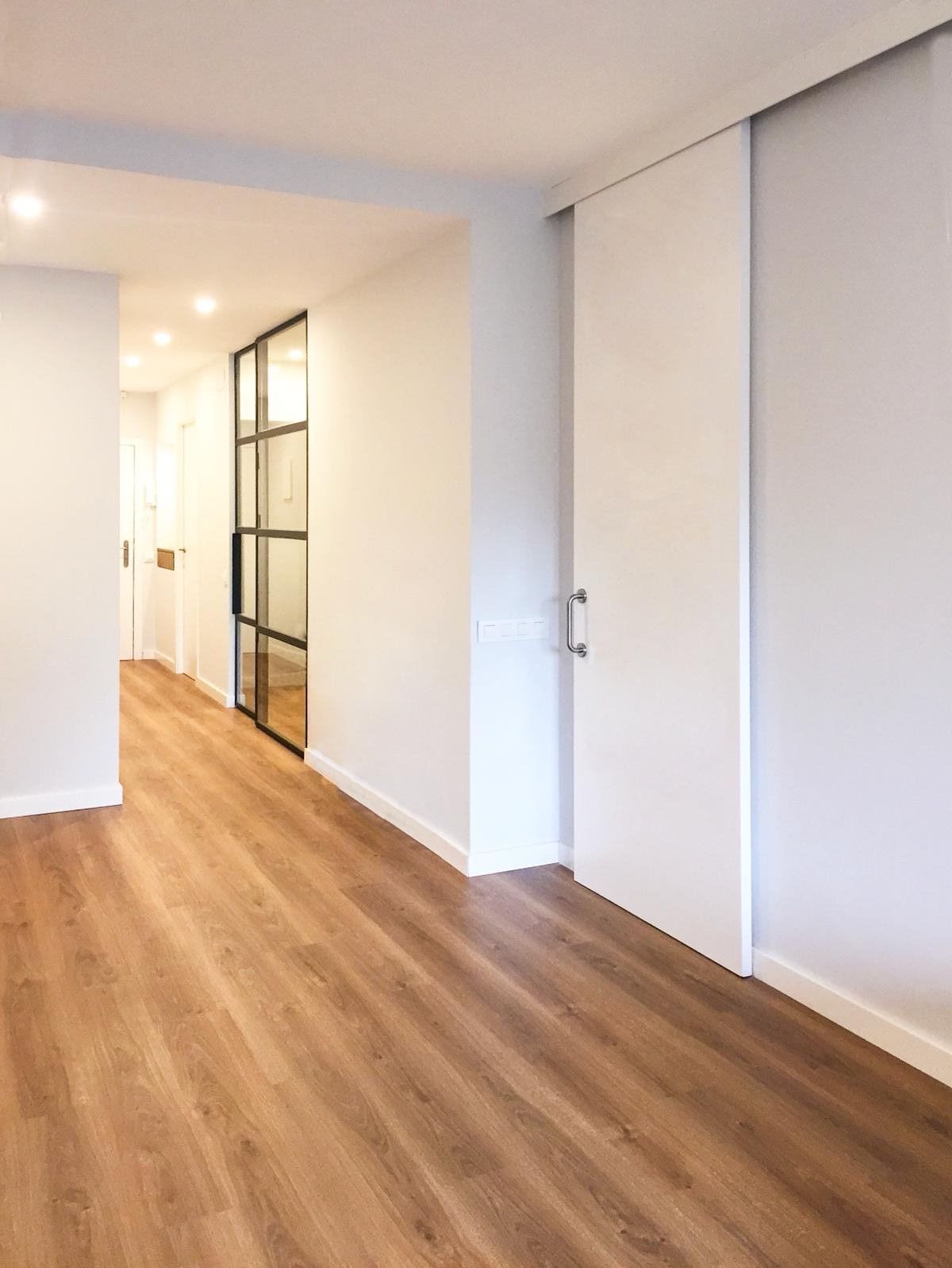 Un pasillo vacío con pisos de madera y paredes blancas.