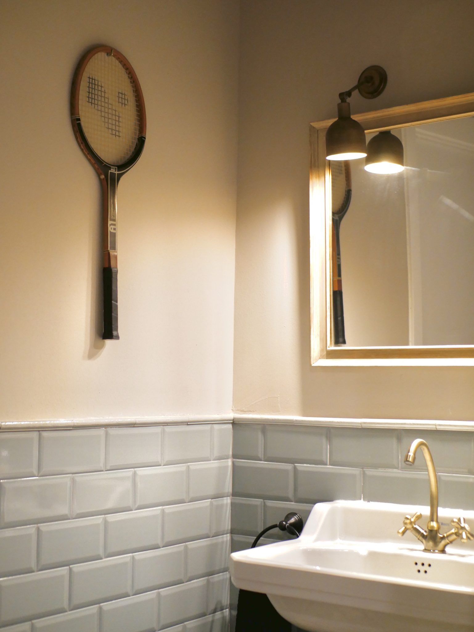 Un baño con un lavabo y una raqueta de tenis en la pared.