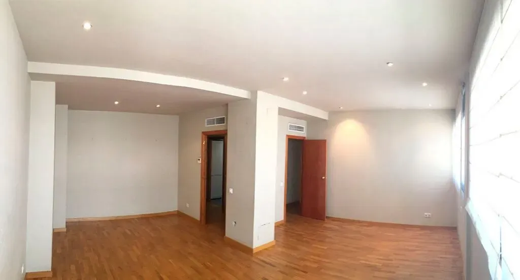 Una sala de estar vacía con pisos de madera y paredes blancas.