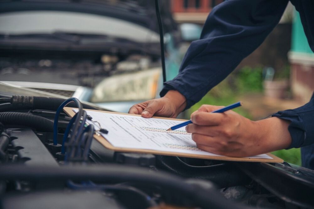 Un mecánico está escribiendo en un portapapeles mientras trabaja en un automóvil.