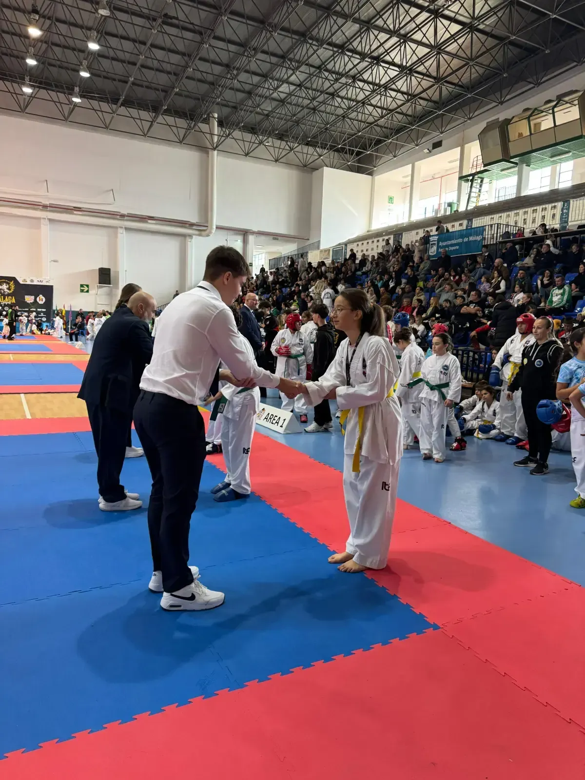 Una persona con camisa blanca estrecha la mano de un artista marcial con uniforme blanco