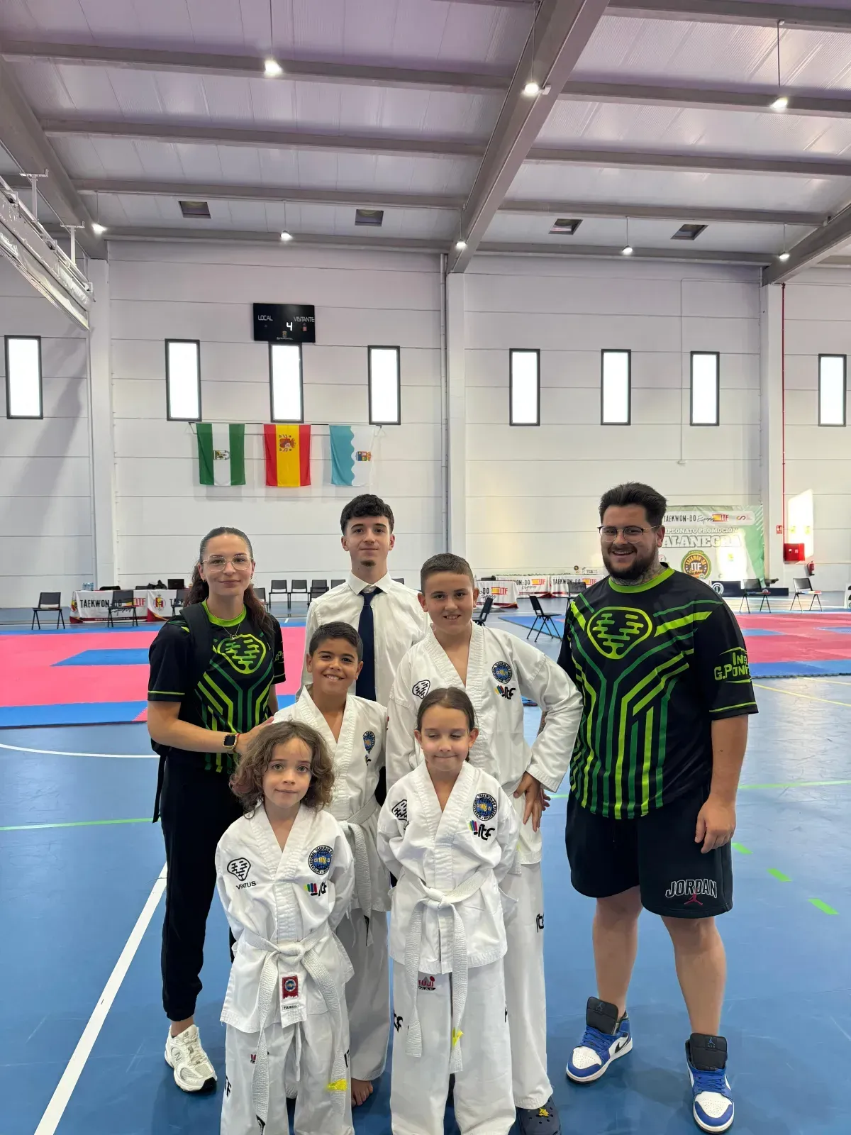 Un grupo de personas con uniformes de artes marciales y camisetas de equipo posan juntas en una luminosa