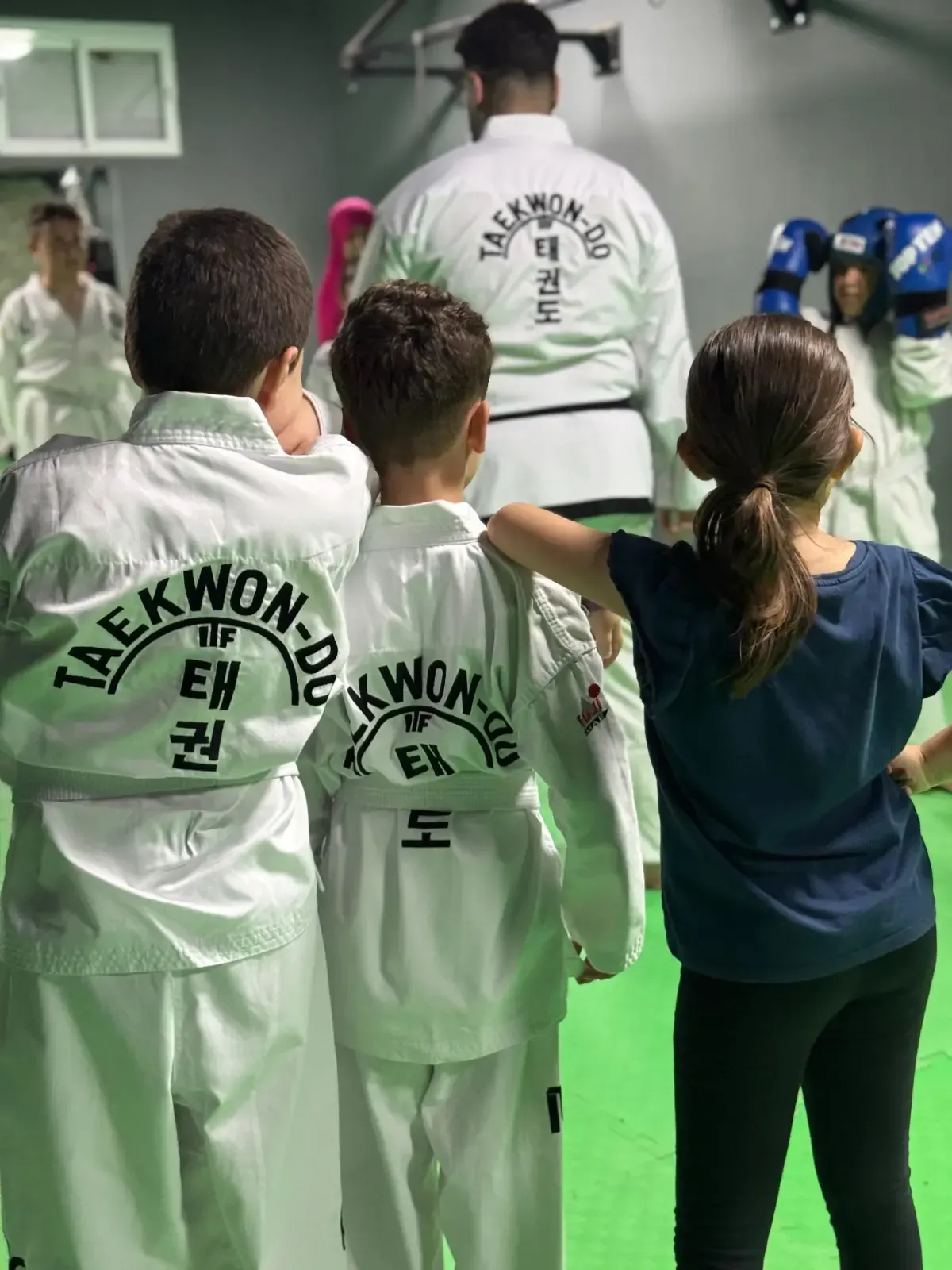 Alumnos con uniformes blancos de Taekwon-Do permanecen de pie en una sala de entrenamiento 