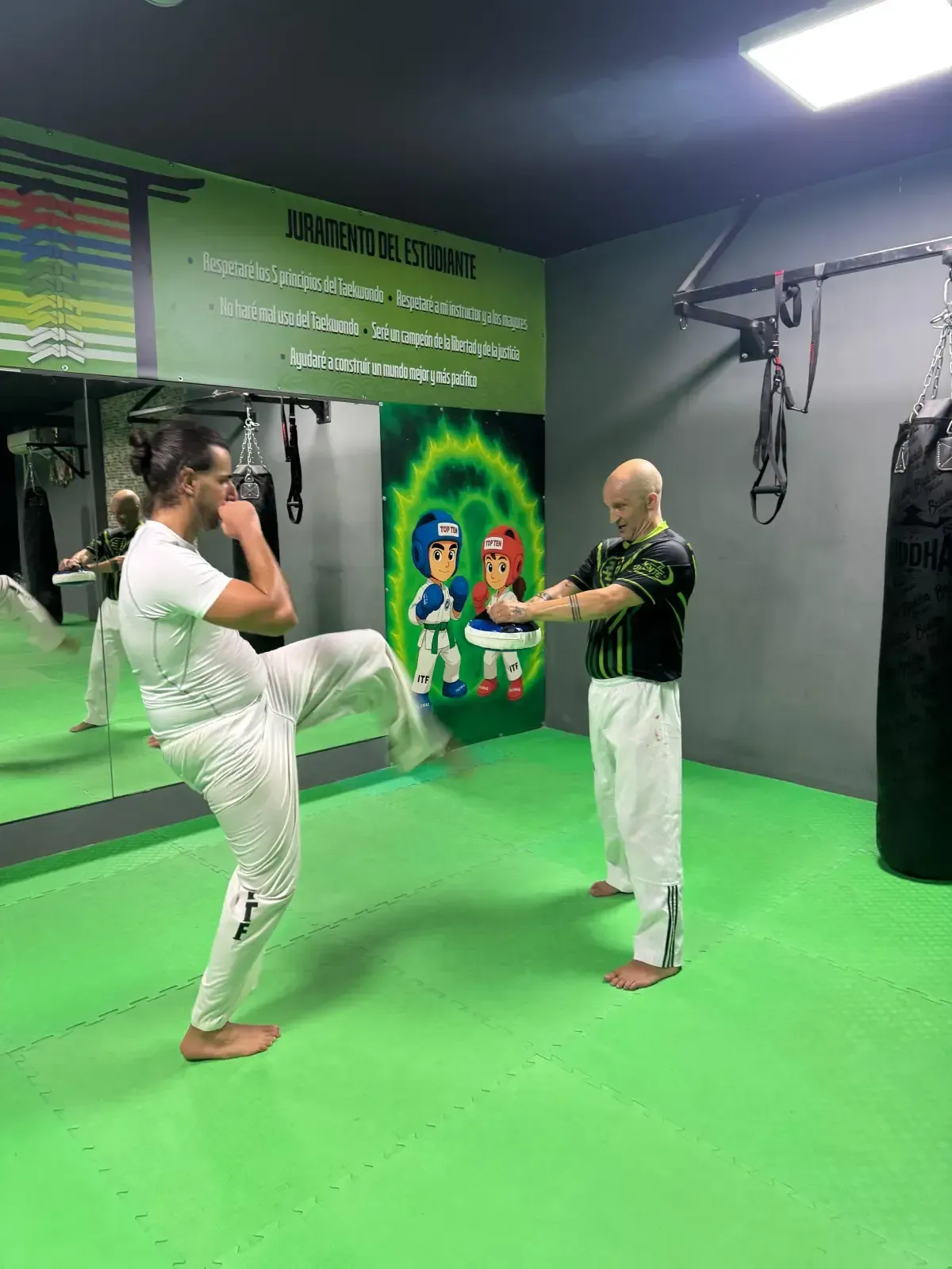 Un instructor de artes marciales le muestra una patada a un alumno en un gimnasio con suelo