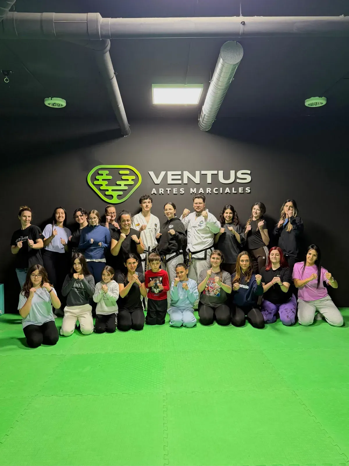 Un grupo de personas de pie en un estudio de artes marciales frente a un letrero de Ventus Artes Marciales.