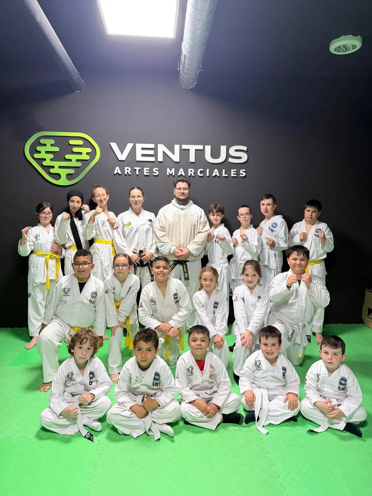 Un grupo de niños y un instructor con uniformes blancos de artes marciales posan sobre una colchoneta
