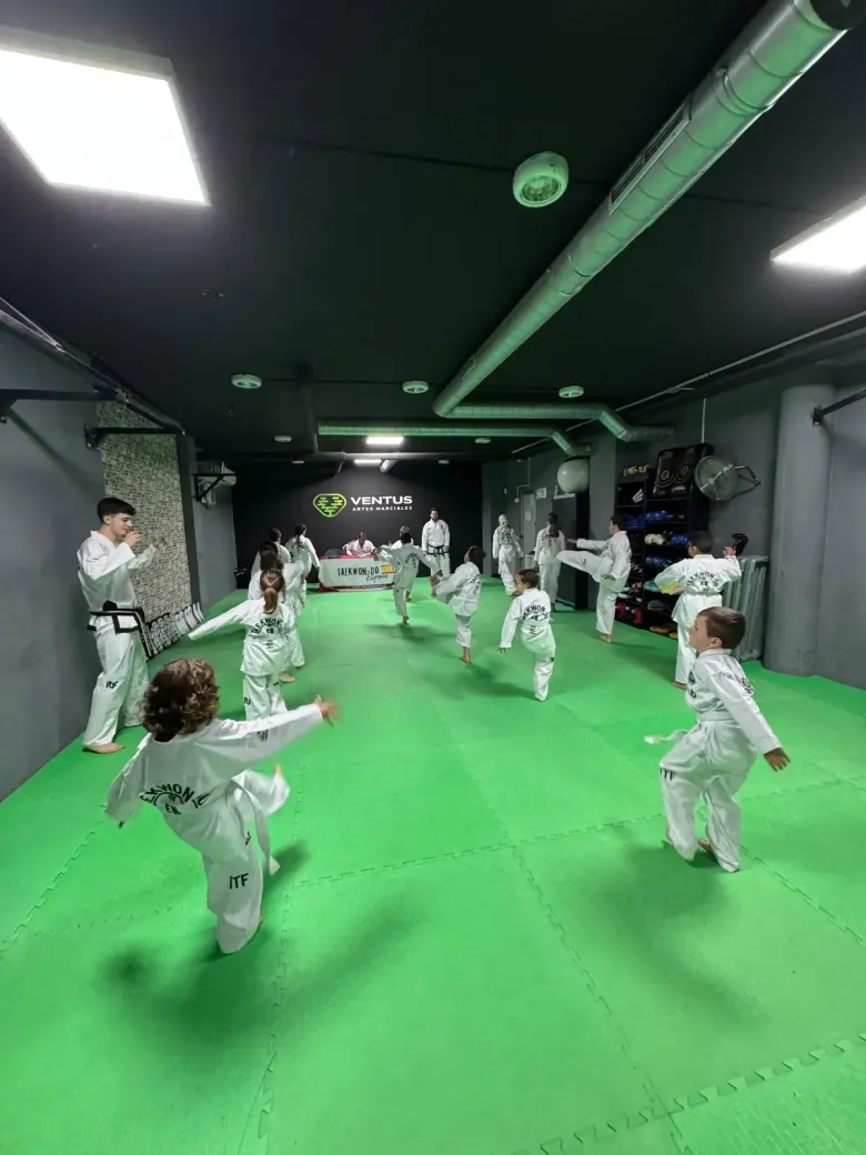 En un estudio de entrenamiento, estudiantes con uniformes blancos practican patadas de taekwondo sobre una colchoneta