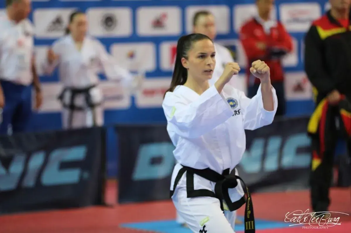 Un atleta de taekwondo con uniforme blanco y cinturón negro se encuentra en posición defensiva