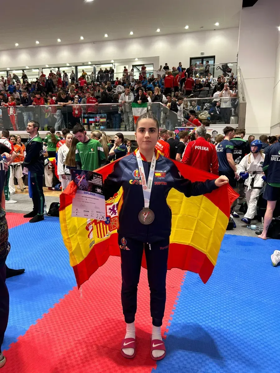 Una persona envuelta en una bandera española se encuentra en un estadio deportivo, luciendo una medalla y sosteniendo 