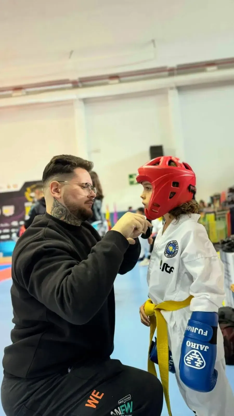 Un instructor ajusta el casco rojo de un alumno en un evento de artes marciales.