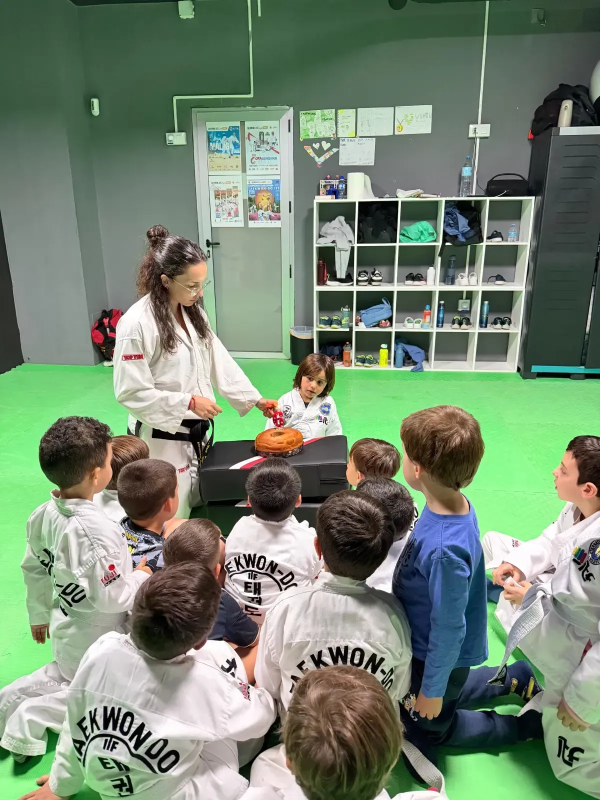 Un instructor de taekwondo muestra una tabla a un grupo de estudiantes en un estudio con suelo verde