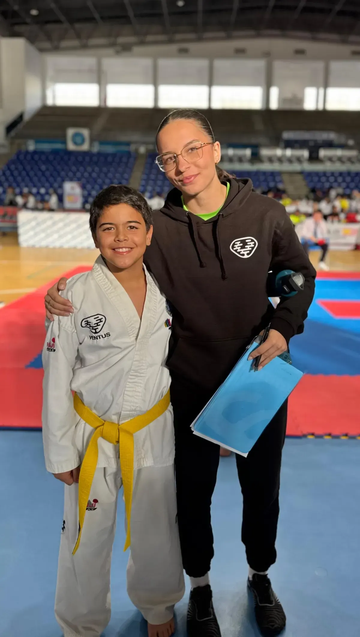Un joven estudiante con uniforme blanco de artes marciales y cinturón amarillo se encuentra junto a un mentor