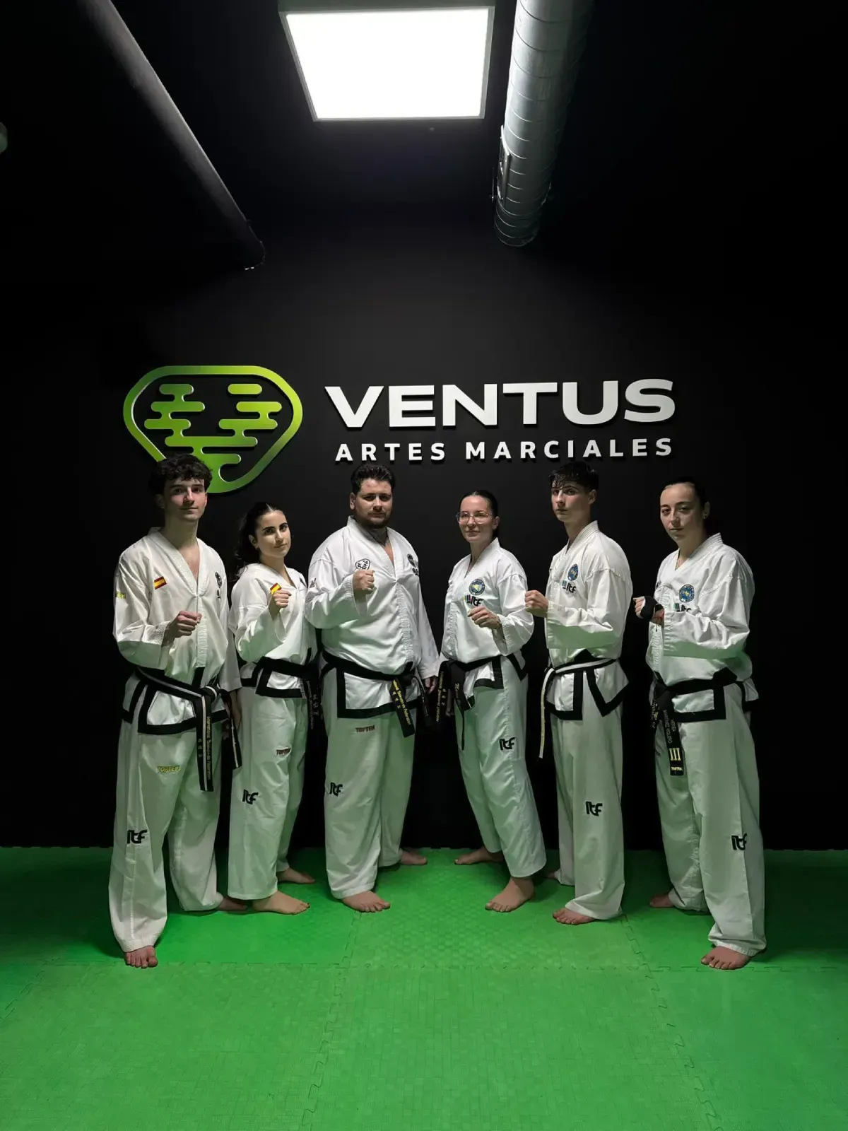 Un grupo de seis personas con uniformes blancos de artes marciales y cinturones negros posan