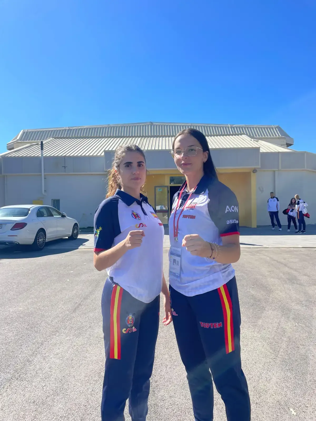 Dos atletas con uniformes de equipo permanecen de pie con los puños cerrados