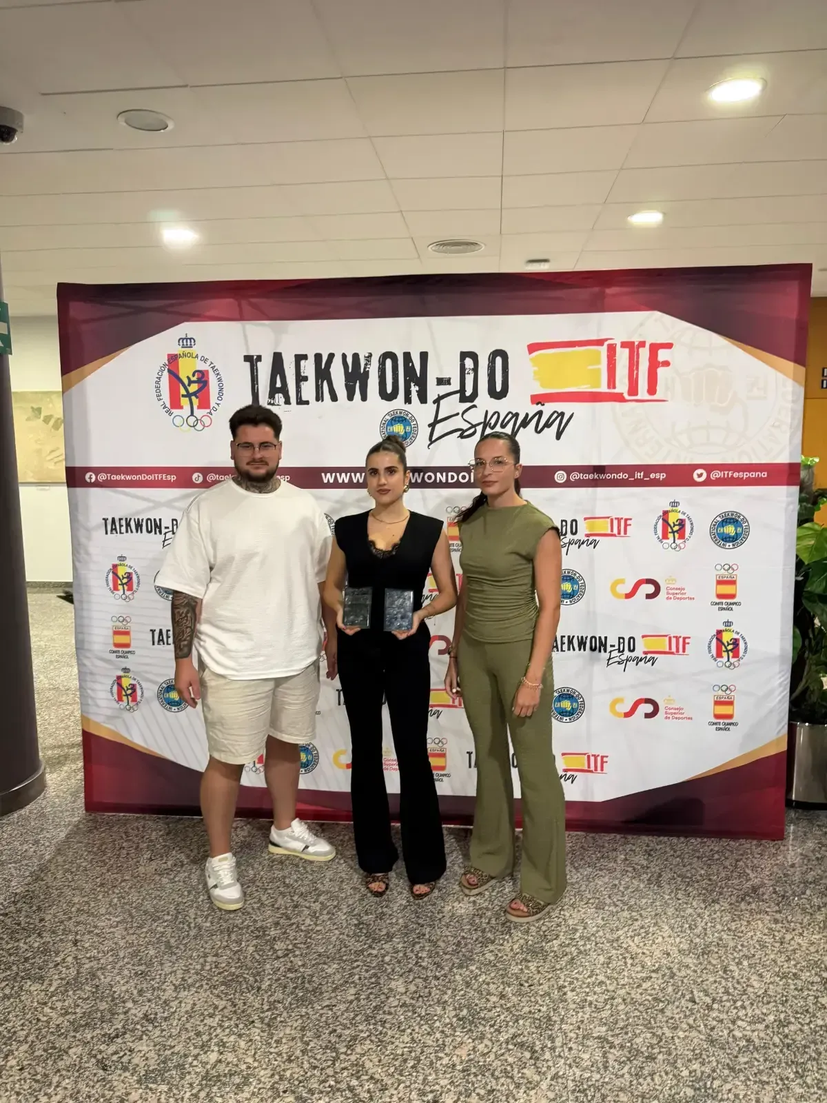 Tres personas se encuentran de pie frente a una pancarta de Taekwon-Do ITF España